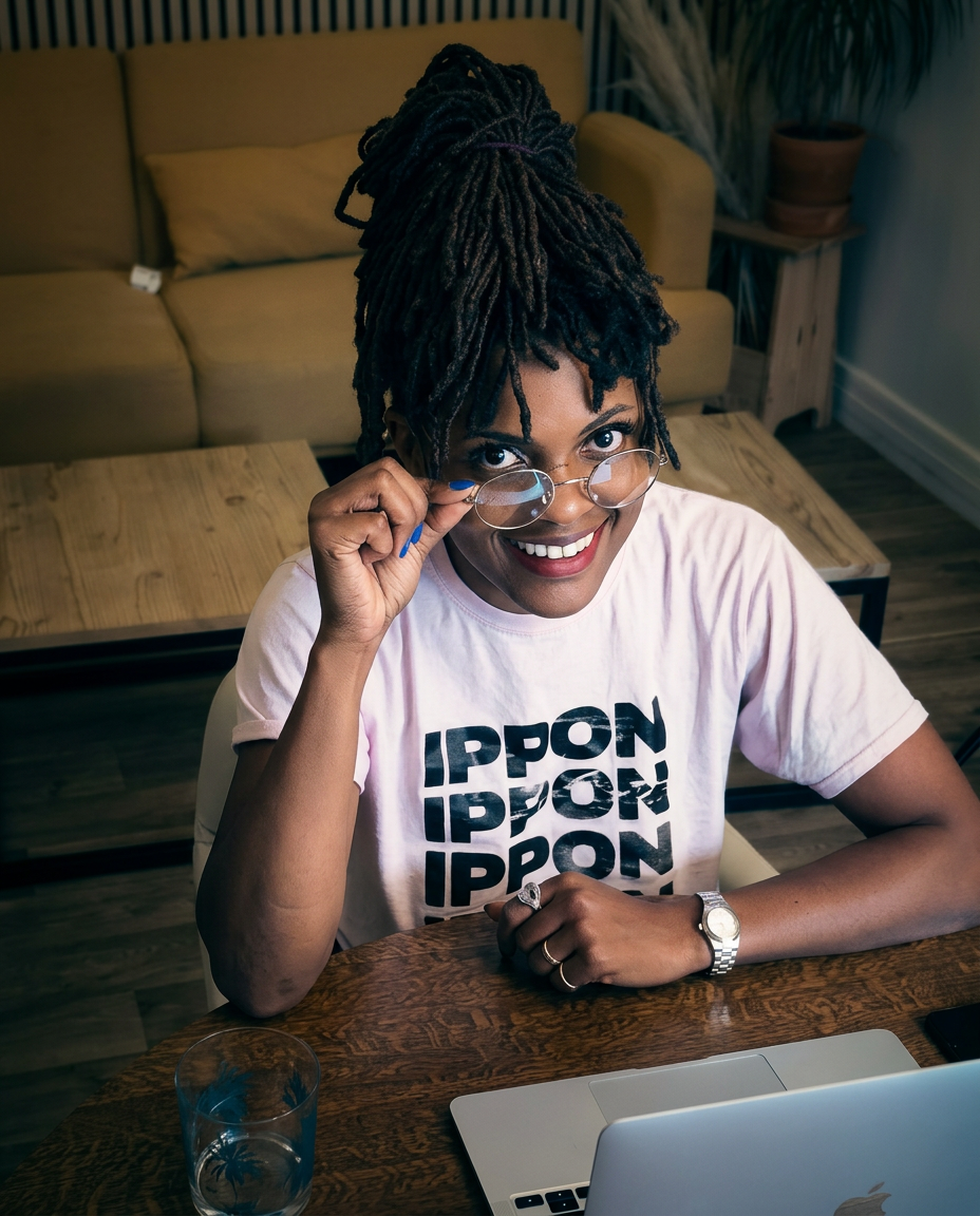 Joanne Selawokah à sa table de travail, lunettes à la main, souriante devant son MacBook